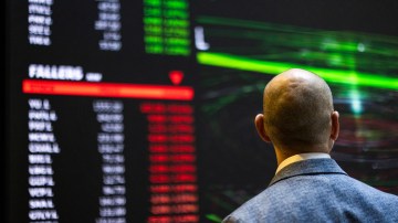 A man in a suit jacket looks at a digital board displaying stock price information.