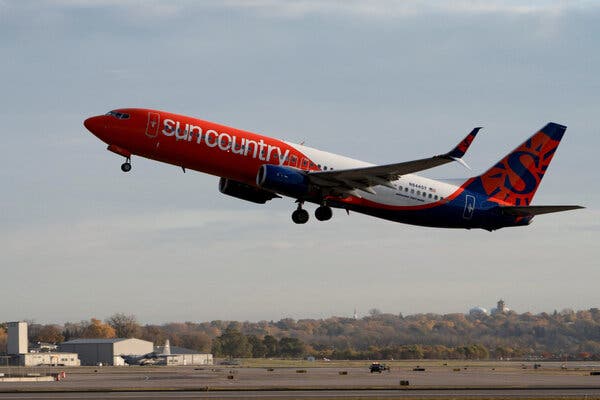 A plane with a Sun Country Airlines logo taking off from an airport runway.