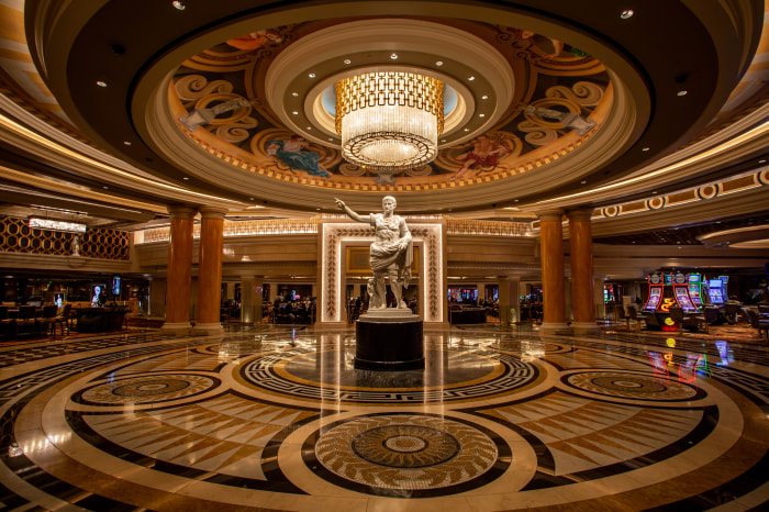 The main entrance of Caesars Palace Hotel & Casino, with a large statue of Julius Caesar in the center, and slot machines visible in the background.
