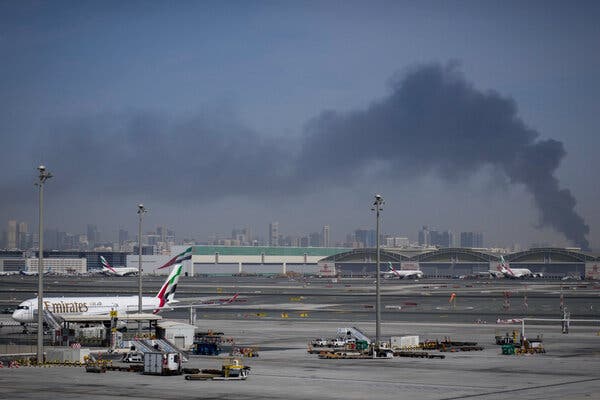 An Emirates plane parked at an airport as black smoke wafts in the background.