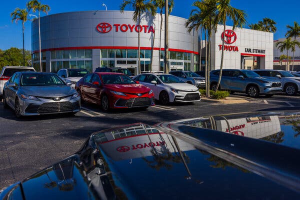 A parking lot outside a Toyota dealership lined with palm trees under a deep blue sky.
